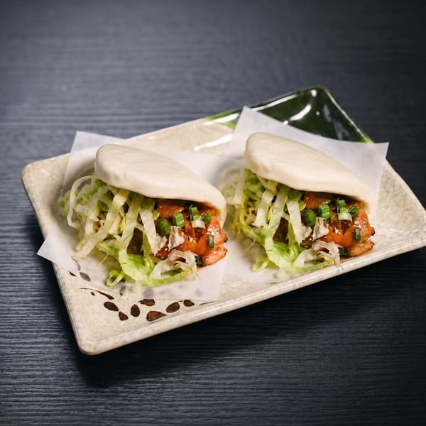 Two bao buns filled with chicken, shredded lettuce, and green onions on a decorative plate.