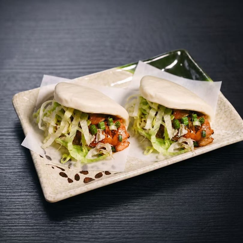 Two bao buns filled with chicken, shredded lettuce, and green onions on a decorative plate.