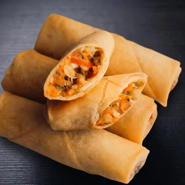 Golden-brown spring rolls, some cut open to reveal a colorful vegetable filling, on a dark surface.